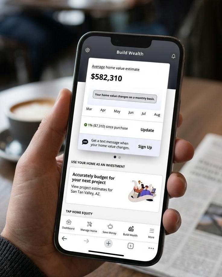 Hand holding a smartphone displaying the Fusion Home Wealth app in a café
